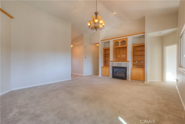 unfurnished living room with built in features, high vaulted ceiling, a tiled fireplace, light colored carpet, and an inviting chandelier