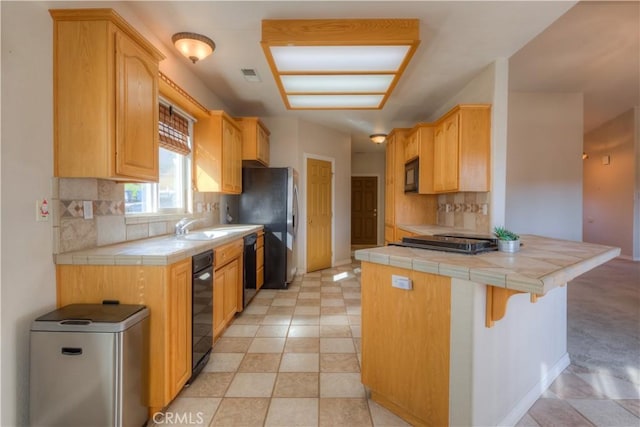 kitchen with tile countertops, black appliances, kitchen peninsula, and light brown cabinets