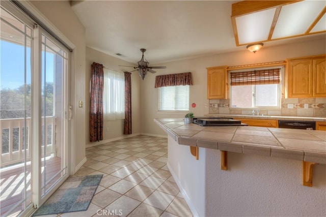 kitchen with a breakfast bar area, black dishwasher, tile counters, decorative backsplash, and light brown cabinets