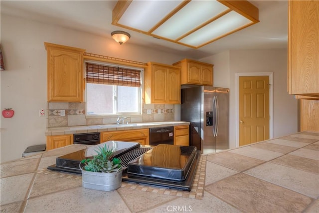 kitchen featuring sink, stainless steel fridge, backsplash, black dishwasher, and tile counters