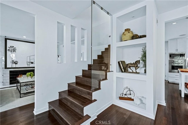 staircase with a tile fireplace, hardwood / wood-style floors, and built in features