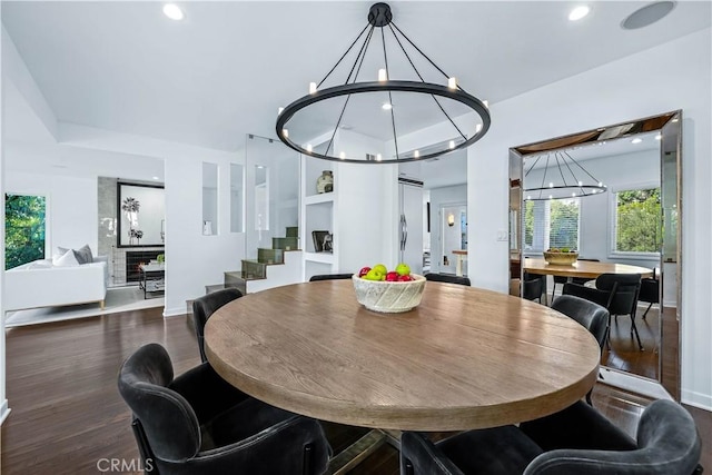 dining area with a notable chandelier, a fireplace, dark hardwood / wood-style floors, and a healthy amount of sunlight