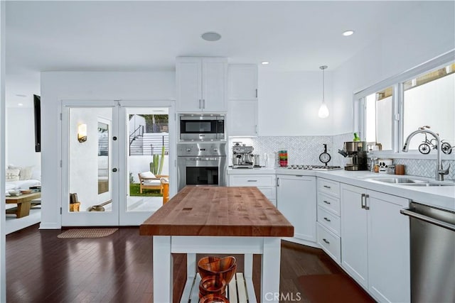 kitchen featuring sink, white cabinetry, hanging light fixtures, stainless steel appliances, and decorative backsplash