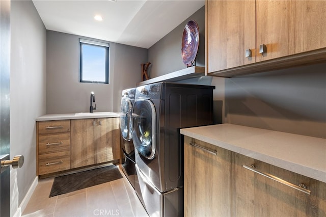 clothes washing area with sink, washing machine and dryer, cabinets, and light tile patterned flooring