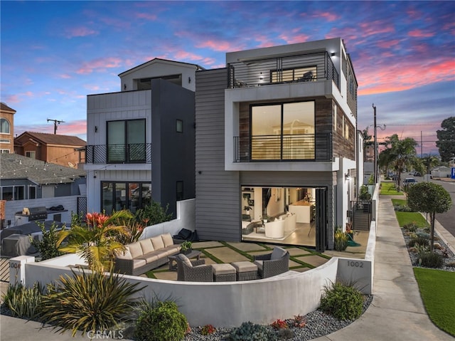 back house at dusk with a patio, a balcony, and an outdoor hangout area