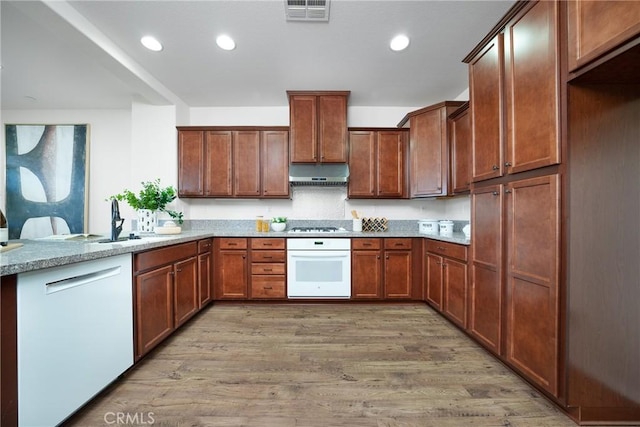 kitchen with sink, white appliances, light stone countertops, and light wood-type flooring