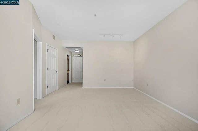 spare room featuring rail lighting and light carpet