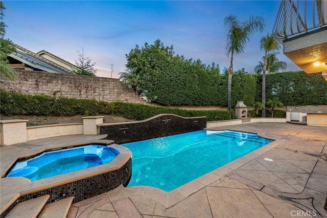 pool at dusk with an in ground hot tub and a patio