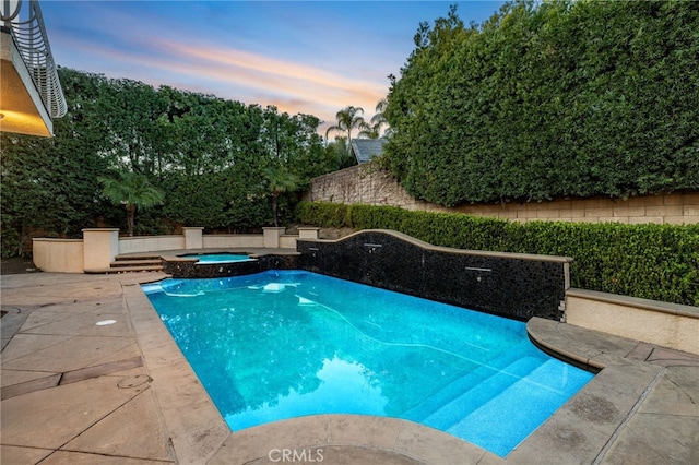 pool at dusk with an in ground hot tub and a patio area