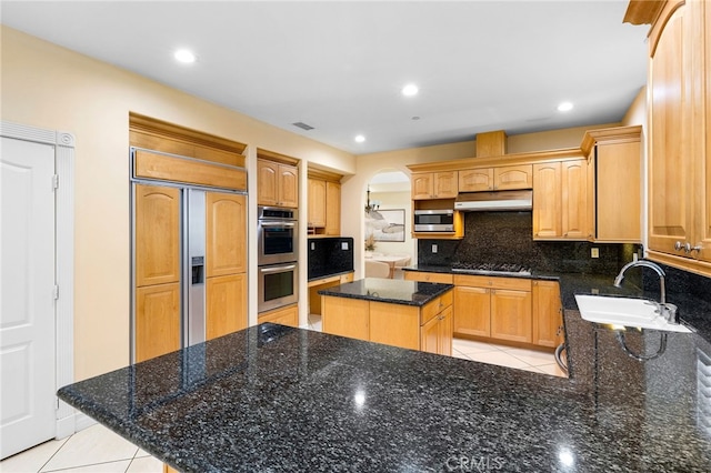 kitchen with sink, stainless steel appliances, a center island, tasteful backsplash, and dark stone counters