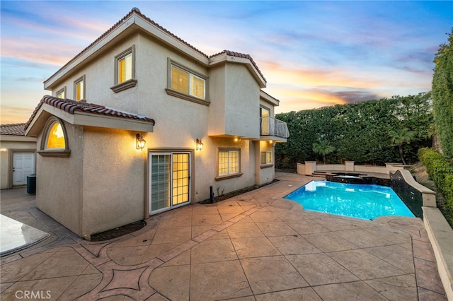 back house at dusk featuring an in ground hot tub, a balcony, a patio, and central air condition unit