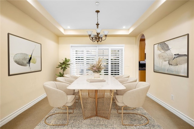 carpeted dining space featuring a tray ceiling and a chandelier