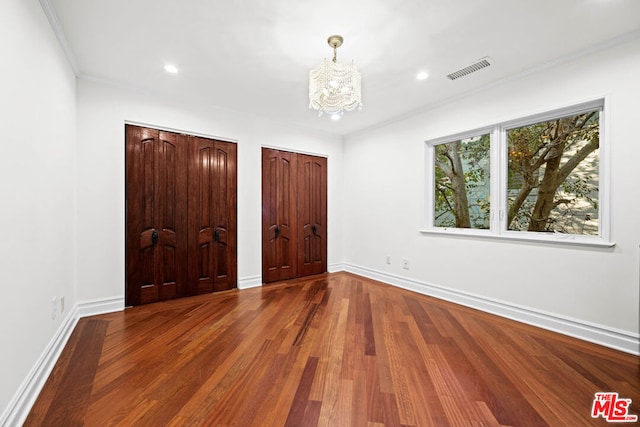 unfurnished bedroom featuring wood-type flooring, a chandelier, and two closets