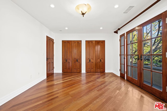 unfurnished bedroom featuring two closets, light hardwood / wood-style floors, and french doors