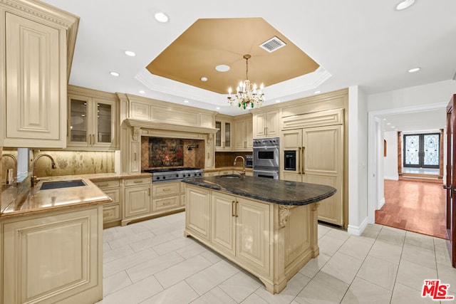 kitchen featuring sink, hanging light fixtures, a center island with sink, a raised ceiling, and backsplash