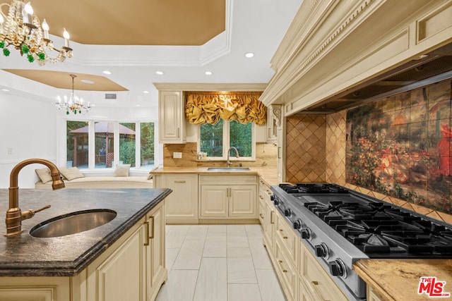 kitchen featuring sink, cream cabinets, stainless steel gas cooktop, a raised ceiling, and a chandelier