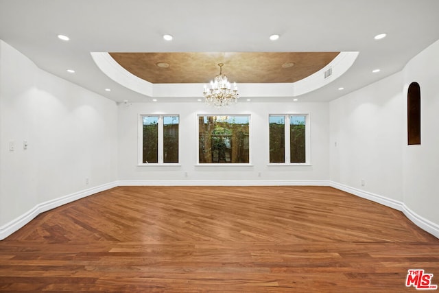 unfurnished room featuring a notable chandelier, a tray ceiling, and parquet floors