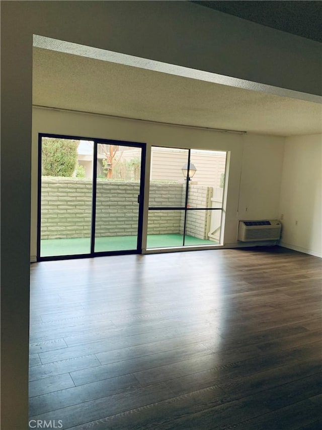 unfurnished room with a textured ceiling, a wealth of natural light, an AC wall unit, and wood-type flooring