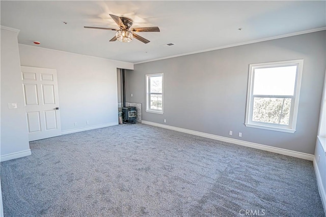 empty room with carpet floors, ornamental molding, a wood stove, and ceiling fan