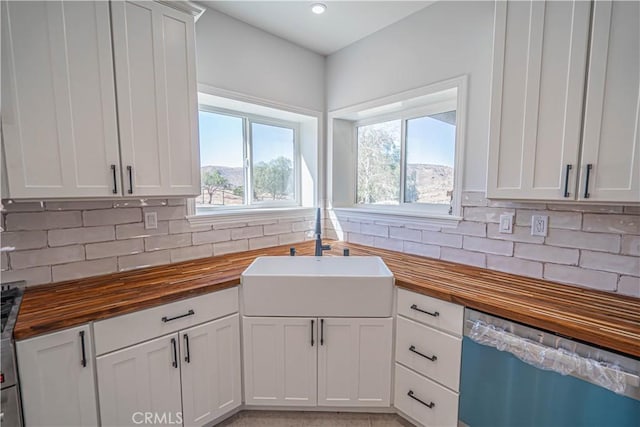 kitchen with stainless steel dishwasher, white cabinets, and wood counters