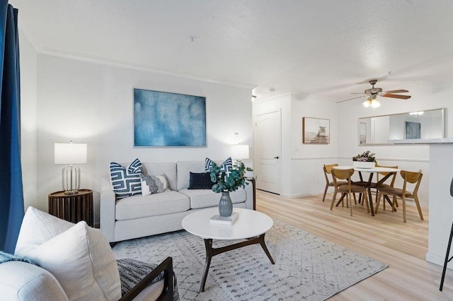 living room with ornamental molding, ceiling fan, and light wood-type flooring