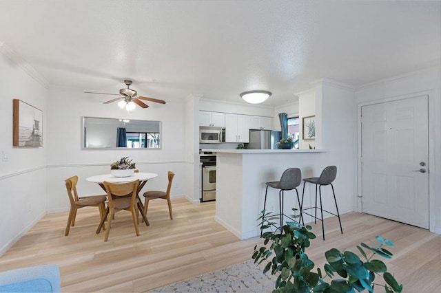 kitchen featuring appliances with stainless steel finishes, a breakfast bar area, white cabinets, kitchen peninsula, and light wood-type flooring