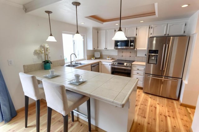 kitchen with sink, appliances with stainless steel finishes, white cabinets, a raised ceiling, and kitchen peninsula