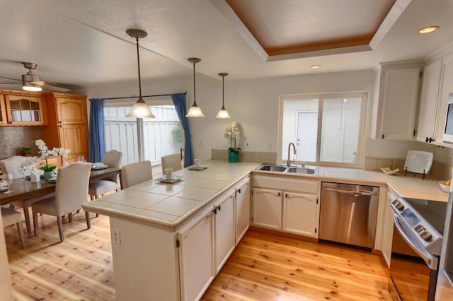 kitchen with hanging light fixtures, stainless steel dishwasher, light hardwood / wood-style floors, kitchen peninsula, and a raised ceiling