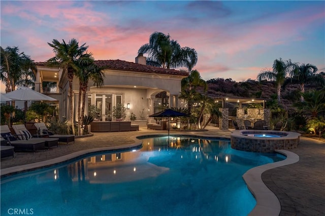 pool at dusk with outdoor lounge area, a patio area, and a pool with connected hot tub