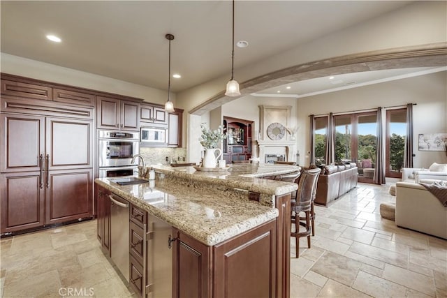 kitchen featuring pendant lighting, sink, built in appliances, light stone counters, and a large island with sink