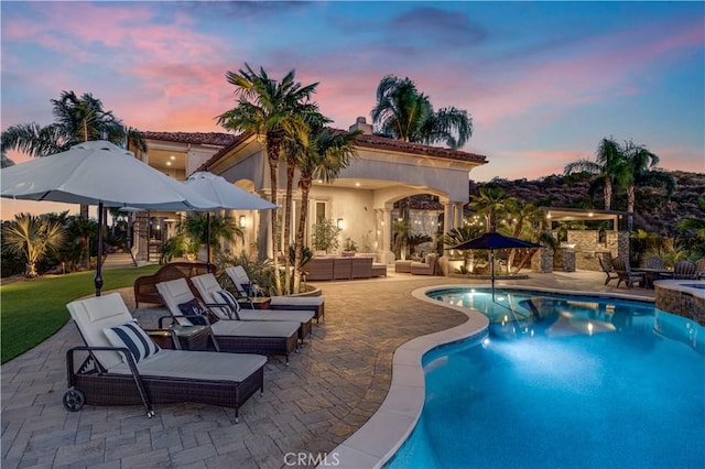 pool at dusk featuring area for grilling, an outdoor hangout area, and a patio area