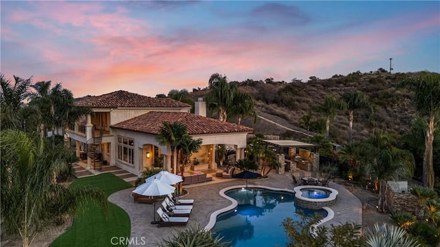 pool at dusk featuring a patio and an in ground hot tub