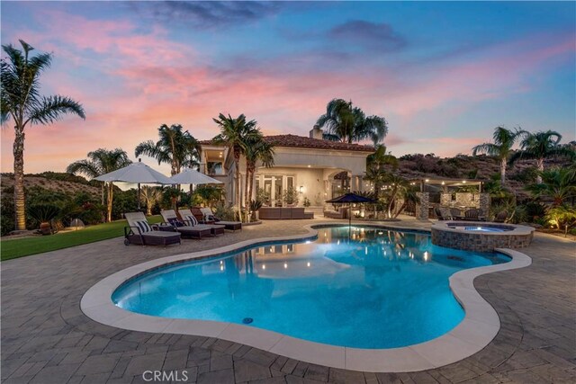 pool at dusk featuring an in ground hot tub and a patio