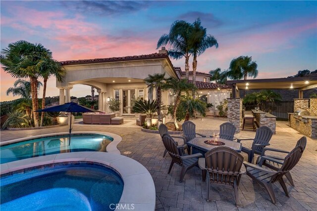 pool at dusk with an in ground hot tub, a patio area, an outdoor living space with a fire pit, and exterior bar