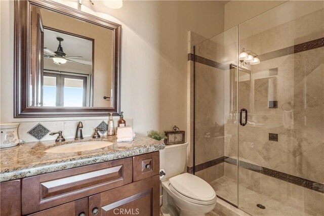 bathroom with a shower with door, vanity, ceiling fan, and toilet