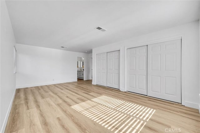 unfurnished bedroom featuring light hardwood / wood-style flooring and multiple closets