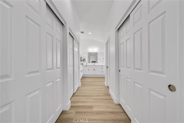 hallway with vaulted ceiling and light hardwood / wood-style flooring