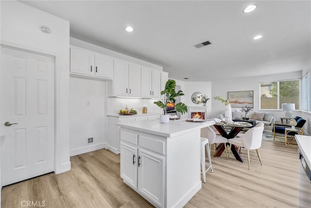 kitchen with light hardwood / wood-style flooring, a center island, white cabinets, and a kitchen bar