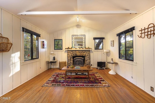 living area featuring lofted ceiling with beams, a healthy amount of sunlight, hardwood / wood-style flooring, and a wood stove