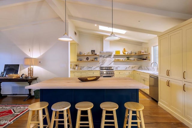 kitchen with appliances with stainless steel finishes, a kitchen bar, decorative light fixtures, and butcher block counters