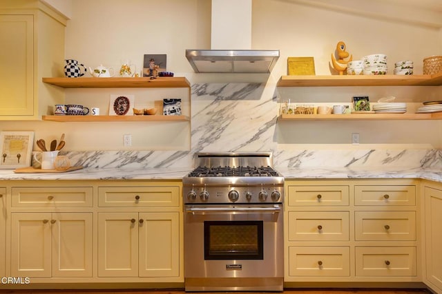 kitchen with cream cabinets, wall chimney range hood, high end stainless steel range, and decorative backsplash