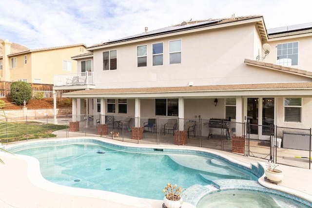 back of house featuring a pool with hot tub, a patio area, and solar panels