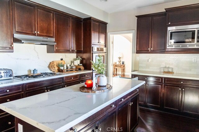 kitchen featuring dark wood-type flooring, stainless steel appliances, a center island, tasteful backsplash, and light stone counters