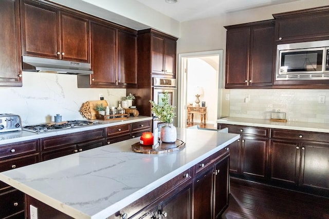 kitchen with dark wood-style flooring, stainless steel appliances, under cabinet range hood, decorative backsplash, and a kitchen island