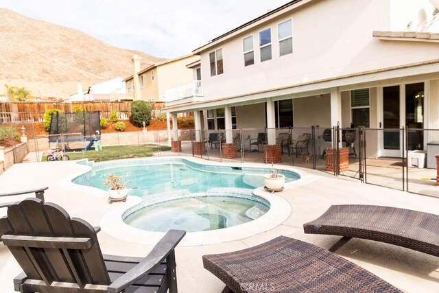 view of pool featuring an in ground hot tub, a mountain view, a trampoline, and a patio area