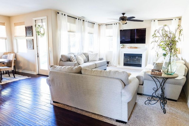 living area with hardwood / wood-style floors, baseboards, ceiling fan, and a glass covered fireplace