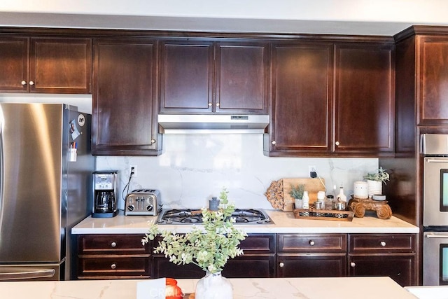 kitchen with dark brown cabinetry, under cabinet range hood, stainless steel appliances, and tasteful backsplash