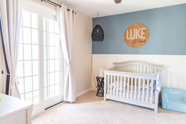 bedroom with carpet floors, a nursery area, and wainscoting