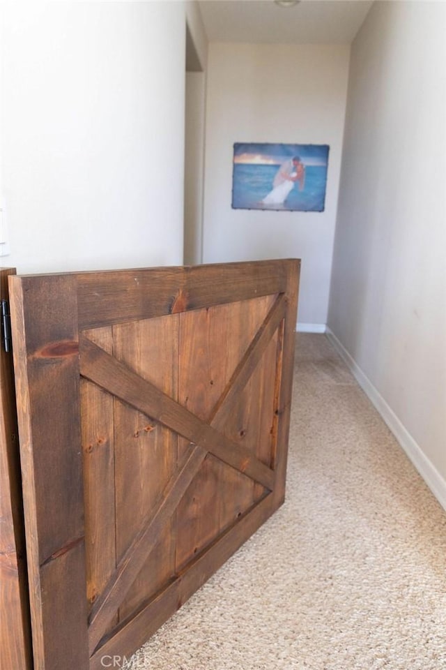 hallway with baseboards and light colored carpet