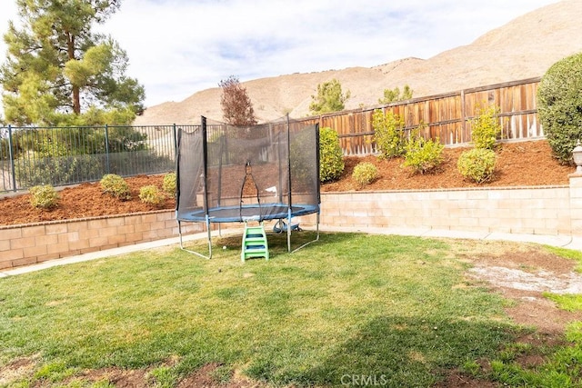 view of yard featuring a trampoline, a mountain view, and fence